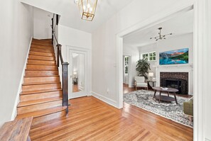 A spacious living area with hardwood flooring, a fireplace, a mounted TV, and a staircase.