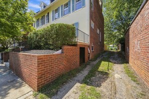 A courtyard with a brick wall, a yellow building with blue shutters, and a tree.