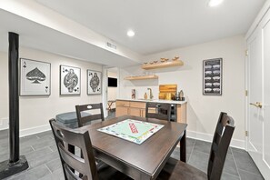 A dining area with a table set for four, a kitchen in the background, and framed playing cards on the wall. - RVA's Muse | 3BR Museum District Retreat (Richmond)