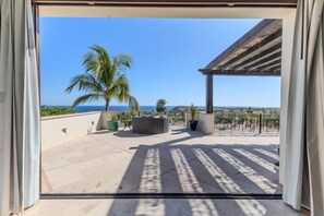 Un patio exterior con vistas al océano, palmeras y una estructura de pérgola.