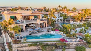 A resort with a swimming pool, lounge chairs, and a landscaped garden. - Casa Alegria | Luxury 6BR Villa | Ocean Views, Infinity Pool & Fire Pit (Cabo San Lucas)