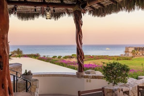 A coastal view with a thatched roof structure, a statue, and a landscaped garden with purple flowers. - Casa Lomboy - Cabo del Sol | 6 Bed, 6.5 Bath (Cabo San Lucas)
