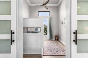 Ein Flur mit Deckenventilator, einem fenster mit Vorhängen, einem gemusterten Teppich und einem kleinen Holzschemel.