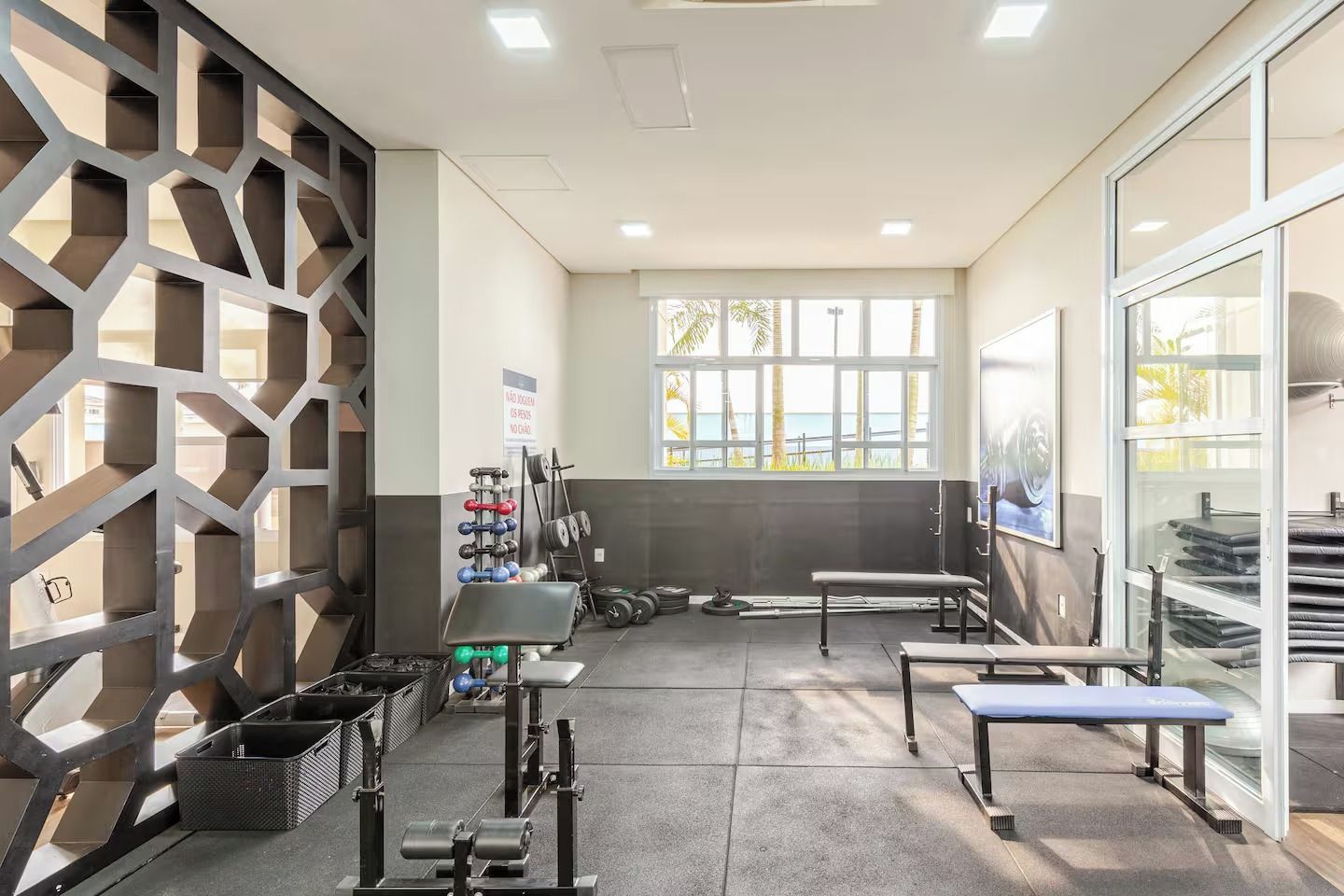 Una palestra con attrezzature per esercizi, panche e vista sull'esterno attraverso ampie finestre.