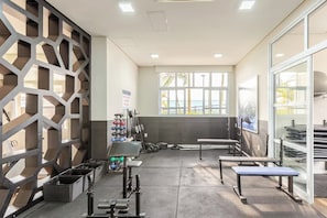 A gym with exercise equipment, benches, and a view of the outdoors through large windows.