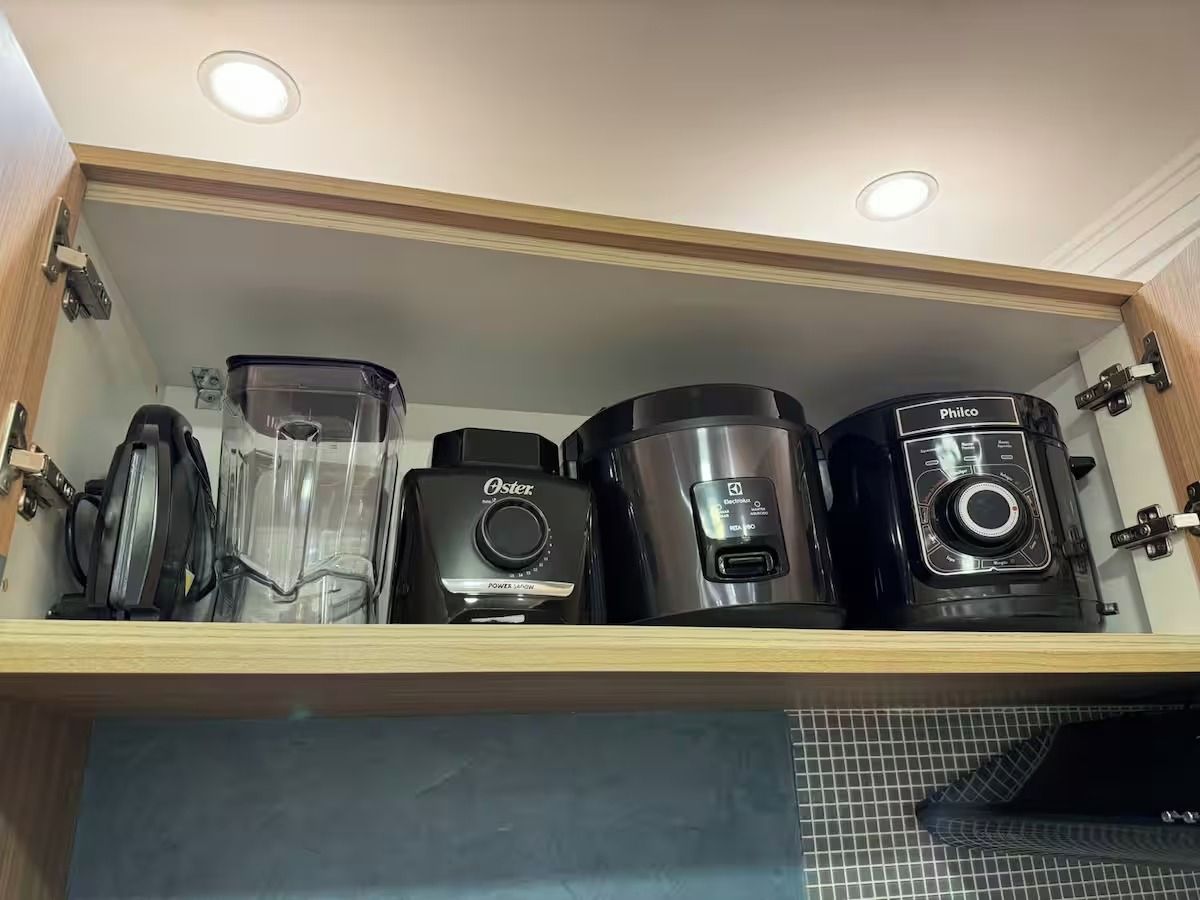 Et køkkenskab med indbygget hylde, der indeholder forskellige apparater, herunder en blender, kaffemaskine og en rislampe.