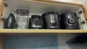 Un armario de cocina con un estante incorporado que contiene varios electrodomésticos, como una licuadora, una cafetera y una cocedora de arroz.