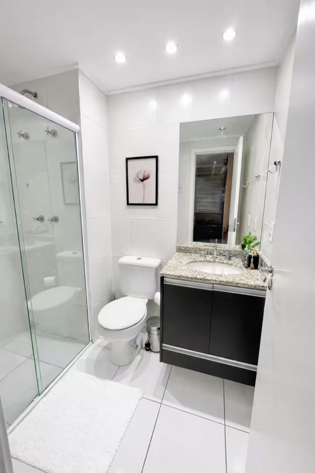 Ein modernes Badezimmer mit Duschkabine aus Glas, einer weißen Toilette, einem Waschbecken mit Granitplatte und einem gerahmten Bild an der Wand.