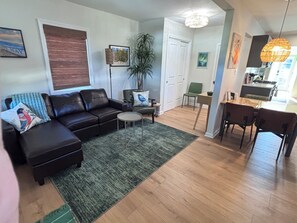 A living room with a black leather sofa, a green rug, and a dining area with a table and chairs. - Cozy 2-bedroom cottage between Wildwood & Cape May NJ (Rio Grande)