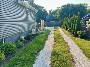 A residential driveway with a 'NO PARKING DRIVEWAY' sign, a gravel path, and a wooden fence with coniferous trees. - Cozy 2-bedroom cottage between Wildwood & Cape May NJ (Rio Grande)