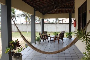 Eine überdachte Terrasse mit einer Hängematte, Holzstühlen, einem kleinen Tisch und Topfpflanzen.