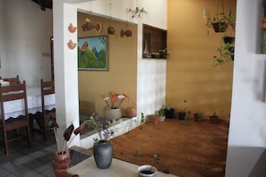 Ein Zimmer mit einem Esstisch, Stühlen, einer Blumenvase, einem Gemälde und mehreren Blumentöpfen.
