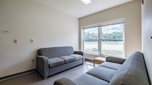 A room with a grey sofa, a small table, and a window with a view of trees and a field.