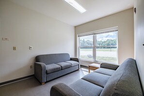 A room with a grey sofa, a small table, and a window with a view of trees and a field.