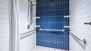 Un baño con paredes de azulejos blancos, una zona de ducha con azulejos azules y suelo de azulejos blancos.