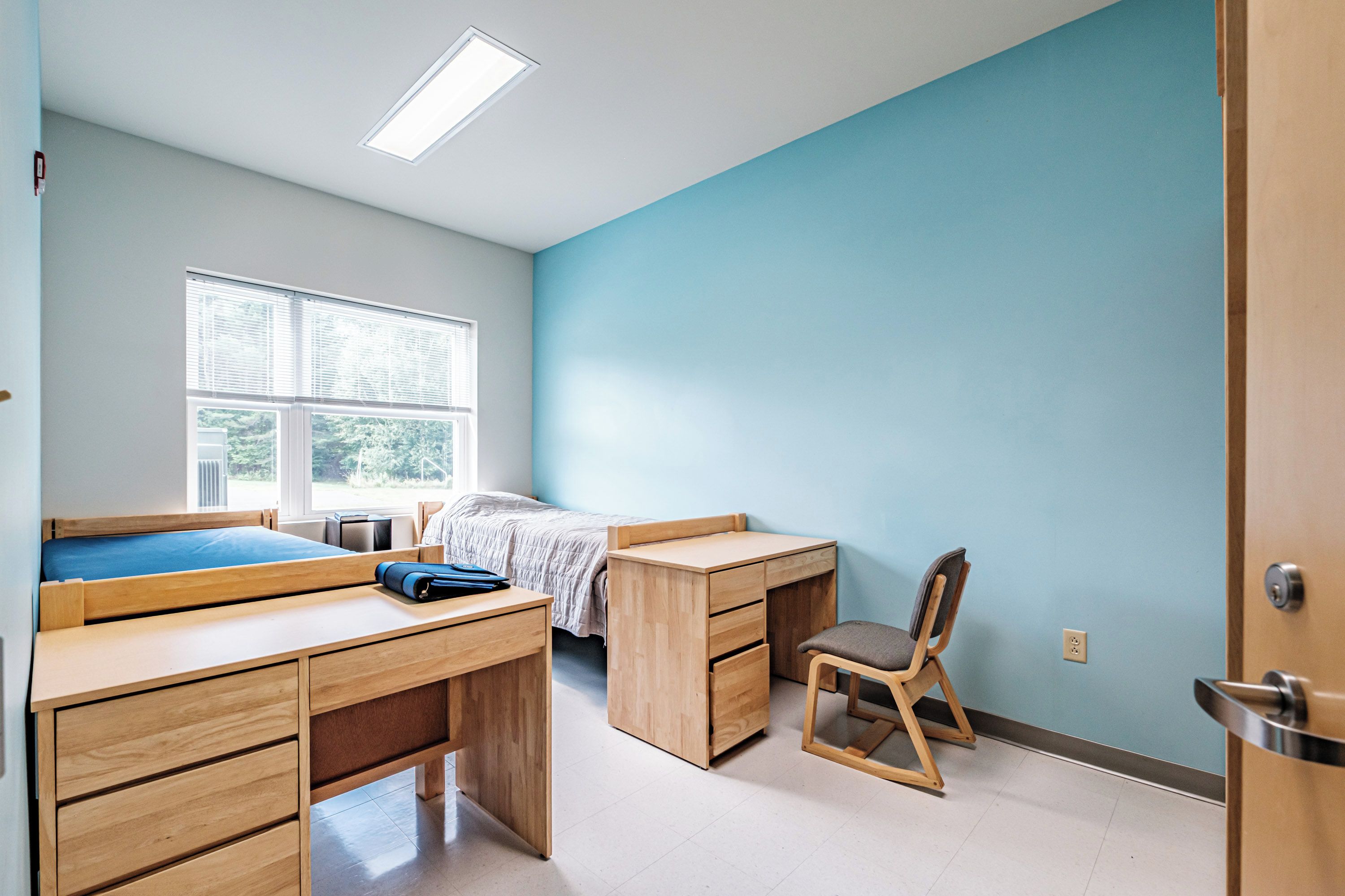Ein Schlafzimmer mit Bett, Schreibtisch, Stuhl und Fenster.