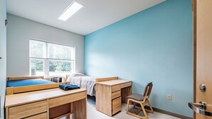 Un dormitorio con cama, escritorio, silla y ventana.
