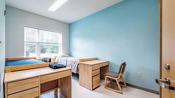 Een slaapkamer met een bed, een bureau, een stoel en een raam.