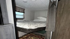 A bunk bed with a lower bunk, a door, and a window with curtains.