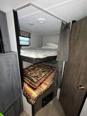Un lit superposé avec un lit inférieur, une porte et une fenêtre avec des rideaux.
