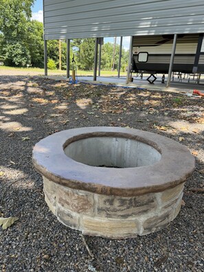 A circular stone fire pit with a metal rim, surrounded by gravel.