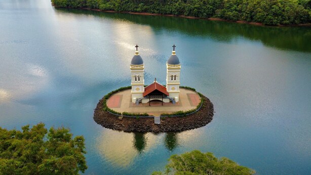 Una isla circular con una estructura central que presenta dos cúpulas y una cruz en la parte superior, rodeada de aguas tranquilas.