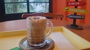 Una taza de vidrio con asa sobre un posavasos, colocada sobre una mesa con vista al exterior.