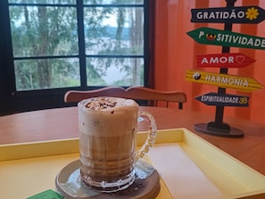 Caneca de vidro com alça sobre um apoio, colocada em uma mesa com vista para a janela.