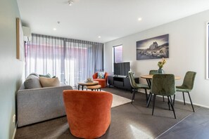 A modern living room with a sofa, a red chair, a dining table with chairs, a TV, and artwork on the wall. - Heart of CHCH - Modern Apt Near Stadium + Parking (Christchurch)