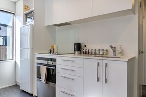Une cuisine moderne avec des meubles blancs, un four encastré, une machine à café et divers ustensiles de cuisine.