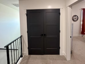 A double door with a black finish, a white wall with a clock, and a carpeted floor. - Pebble Brooke Place- Brand New Townhouse- easy access to National Parks! (Rexburg)