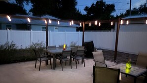 Een terras buiten met een tafel en stoelen, sfeerverlichting en een overdekt gedeelte.