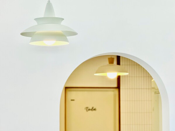 Un intérieur blanc avec un luminaire au plafond et une porte en arc donnant sur une pièce dont la porte est marquée de l’inscription « Villa ».