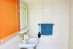 Casa de banho com lavatório branco, espelho e toalheiro com toalha azul.