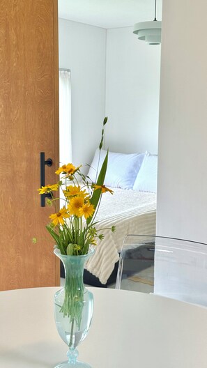 Quarto com cama, mesa de cabeceira com um vaso de flores e porta de madeira.