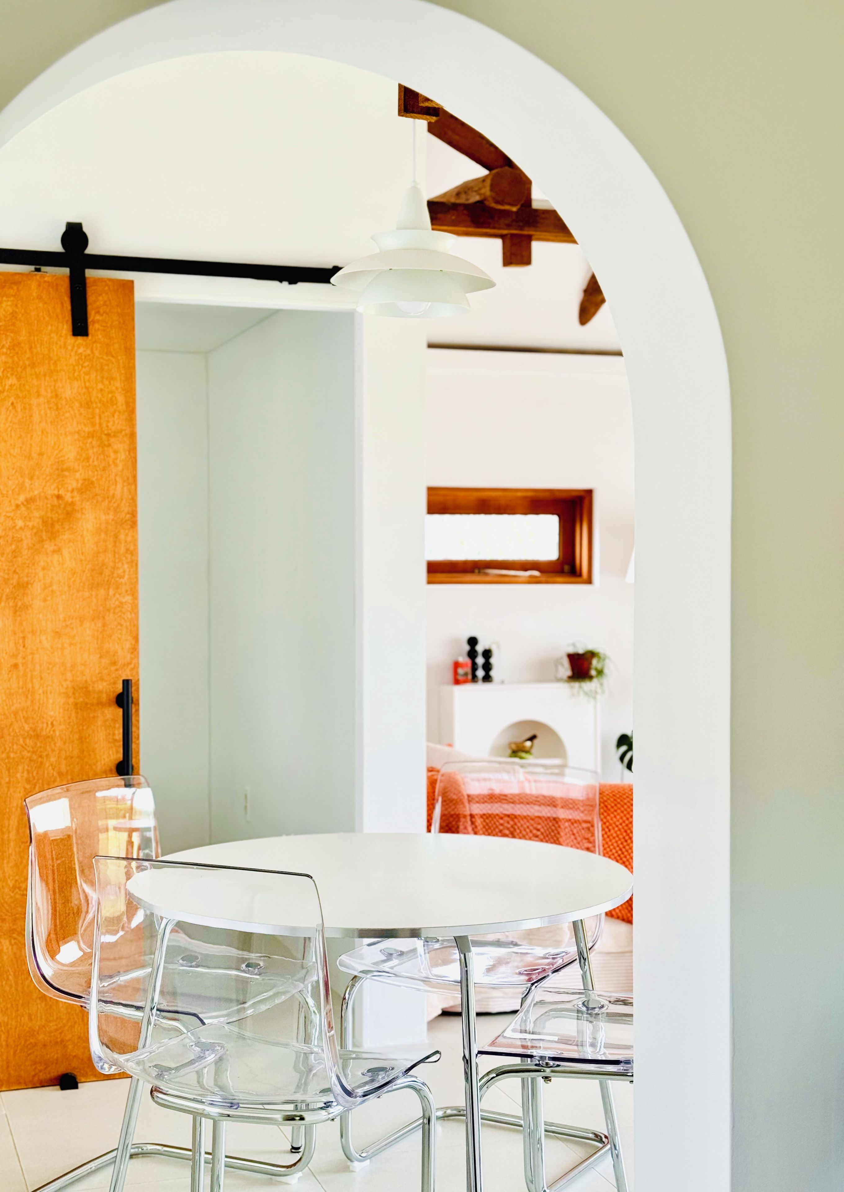 Un espace repas avec une table ronde, des chaises transparentes et un luminaire suspendu.
