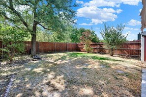 A backyard with a wooden fence, a tree, and a grassy area. - New! Luxury Spacious Home 4 Beds 2 Bath 20 Min DTX (Balch Springs)