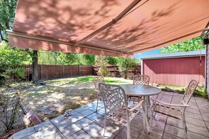 Eine Terrasse im Freien mit Tisch und Stühlen, einem überdachten Bereich und einem Holzzaun im Hintergrund.