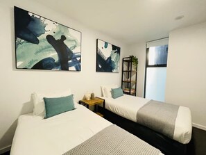 Una camera d'albergo con due letti, un comodino, una libreria e quadri astratti alle pareti.