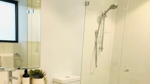 Et moderne badeværelse med brusekabine i glas, et hvidt toilet og en vask med spejl over.