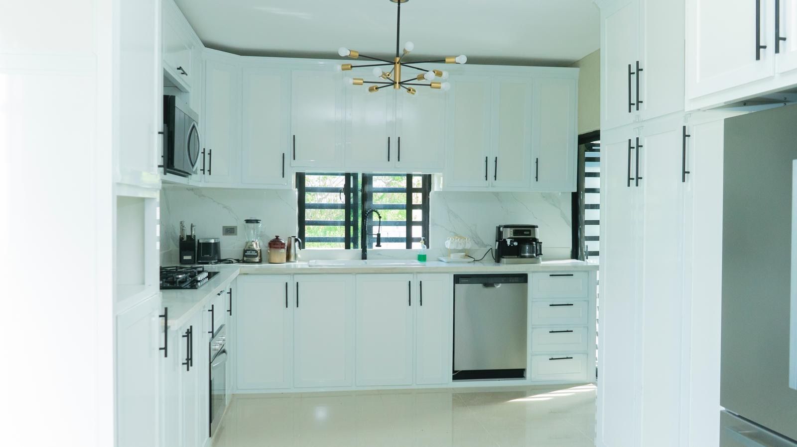 A modern kitchen with white cabinetry, a built-in dishwasher, and a coffee maker.