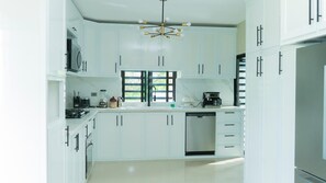 A modern kitchen with white cabinetry, a built-in dishwasher, and a coffee maker.