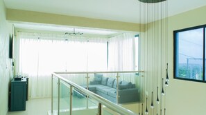 A modern living room with a glass railing, a grey sofa, and a view of the outdoors.