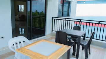 A balcony with a table and chairs, a sliding glass door, and a view of greenery.