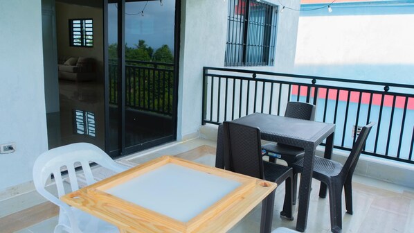 A balcony with a table and chairs, a sliding glass door, and a view of greenery.