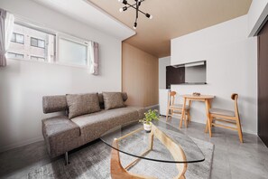 Ein stilvoller Wohnraum mit einer Couch, einem kleinen Tisch mit Pflanze und einem an der Wand befestigten Fernseher.