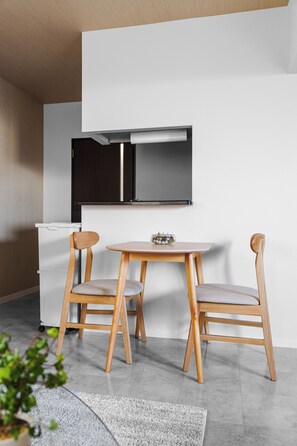 A modern kitchen with a white countertop, two wooden chairs, a round table, and a built-in black oven. - Anax Nord 103 (Sapporo)