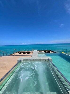 Ein Poolbereich mit klarem Wasser, einer Holzterrasse und Blick auf den Ozean.