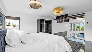 A modern bedroom with a large bed, a ceiling fan, a TV, and a balcony with a pool view.