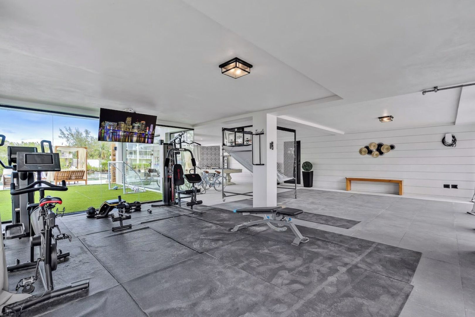 A modern home gym with exercise equipment, a large TV, and a view of a green lawn.